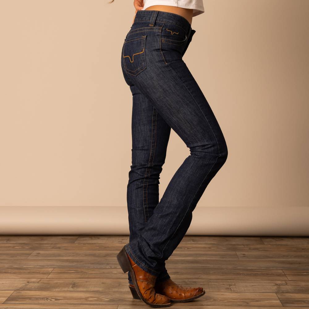 Woman wearing Kimes Ranch Sarah jeans in a dark wash, styled with brown cowboy boots and a white top. The jeans feature the signature longhorn stitching and a flattering slim fit through the leg.