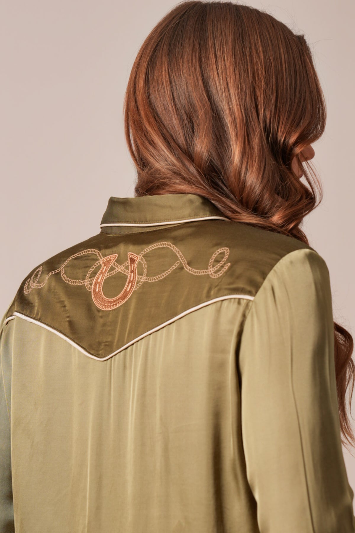 Kimes Ranch Merada top in Moss shows a yoke with white piping and an embroidered horseshoe design on the back