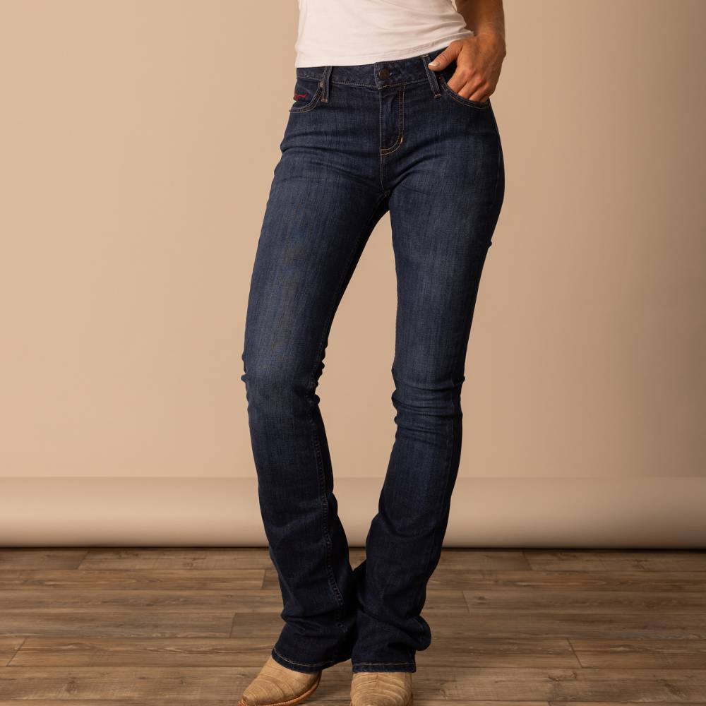 Woman wearing Kimes Ranch Chloe jeans in a dark wash with hand-sanded details and a modest-flare bootcut leg. The mid-rise jean features a fitted thigh and a burgundy horn logo on the back pocket, offering a flattering Western riding fit.