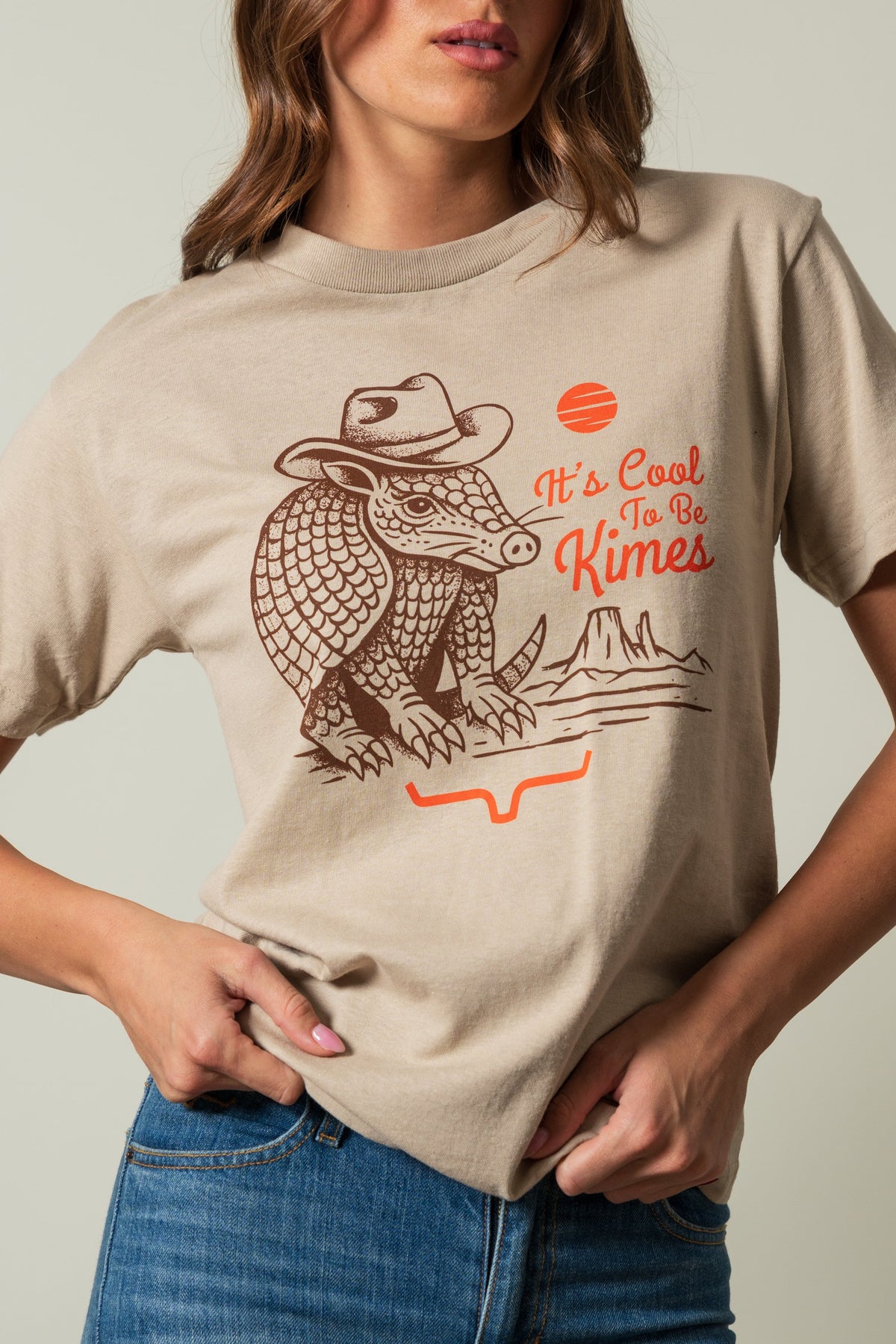 Kimes Ranch Dillo shirt in Sand, featuring an armadillo in a cowboy hat with "It's Cool To Be Kimes" text and orange accents; #color_sand